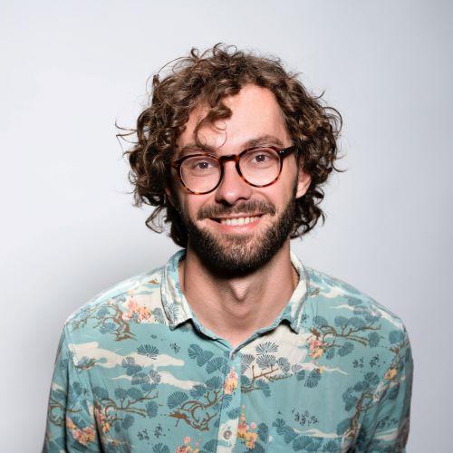 a profile picture of a man with brown curly hair and glasses