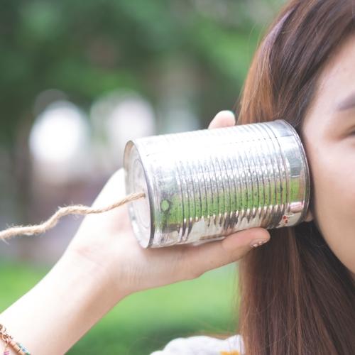 a young girl holding up a home made tin and string phone to her ear