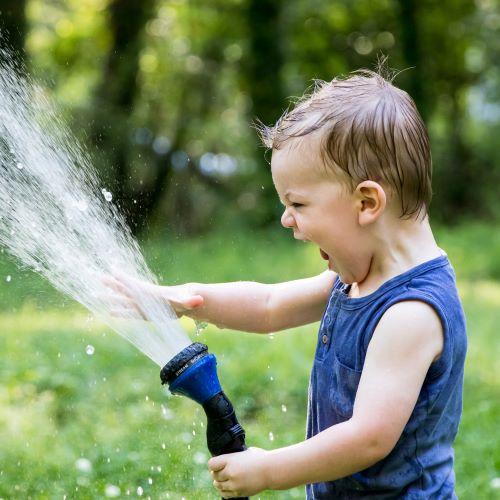 a young boy holding up a hose pipe and spraying water